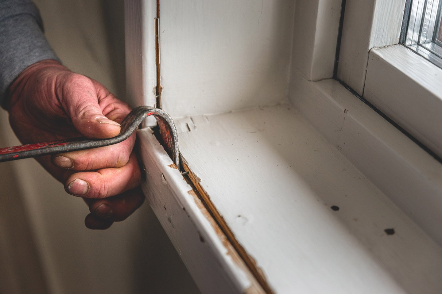 Nærbilde av hånd med verktøy som fjerner gamle tetningslister fra vinduskarm.