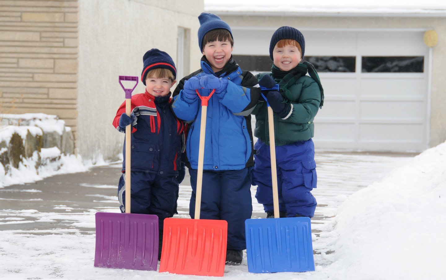Tre små barn med snøskuffer