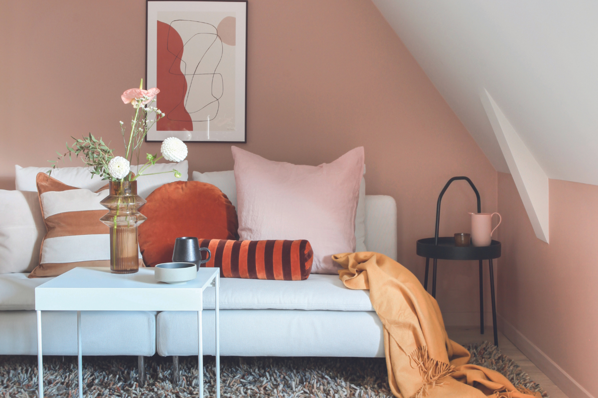 Stue med vegger malt i dempet rosa, kombinert med fargerike puter, pledd og dekorasjoner.