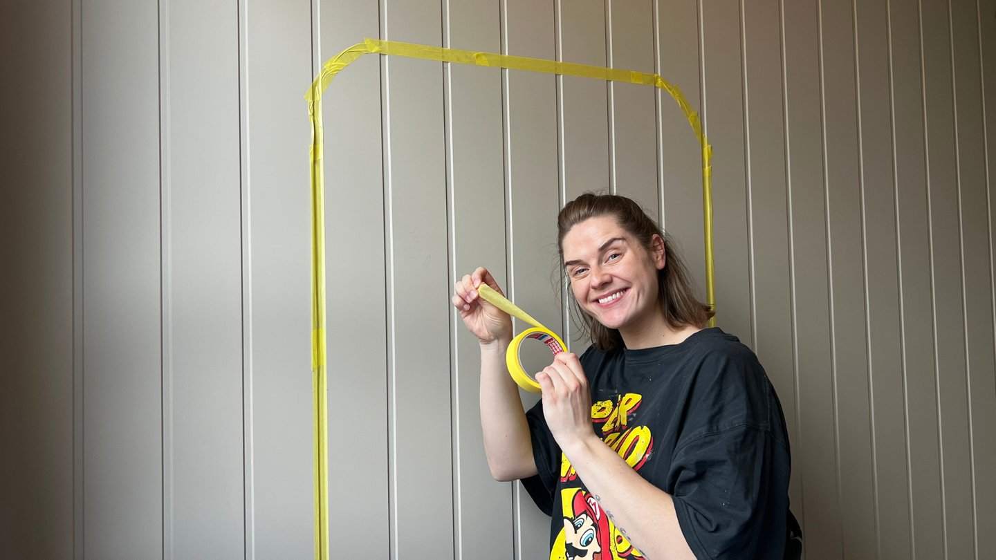 Smilende kvinne bruker gul maskeringstape på veggen.