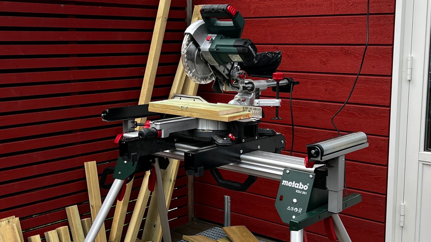 Kapp- og gjærsag ute med materialer klare til skjæring, foran et rødt hus.