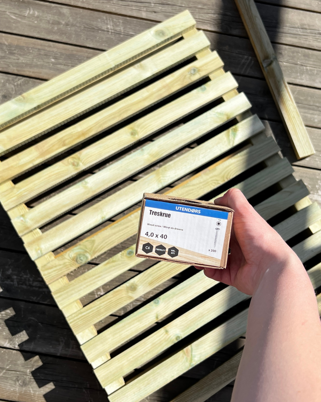 Kvinne holder Treskruer (4,0 x 4,0) i boks, over tredør av spiler