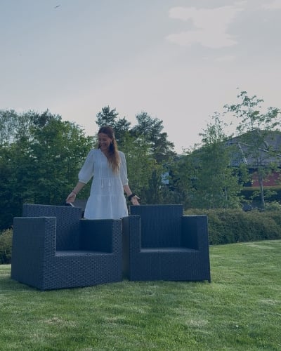 En dame som står på en gressplen, med to stoler i rotting foran seg.