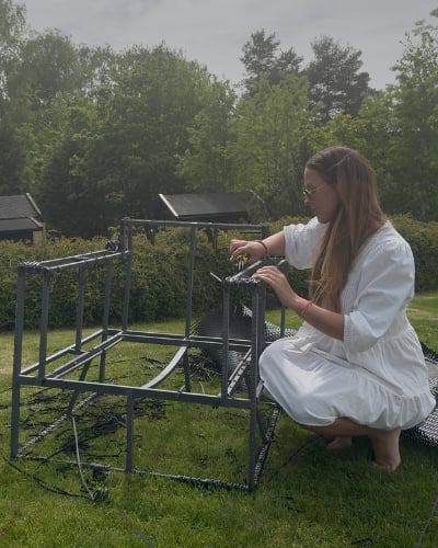 En kvinne som sitter på en gressplen med et møbel hun tar ut gamle skruer fra.