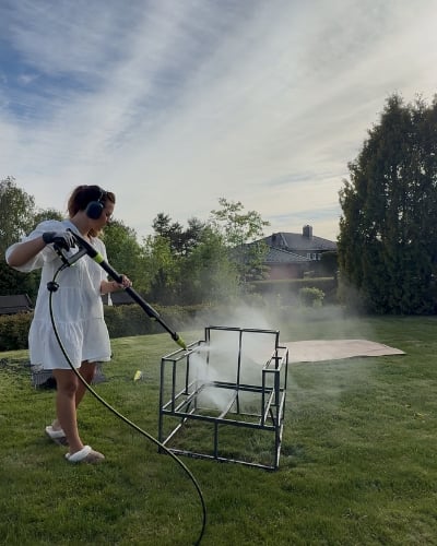 En kvinne som spyler et møbel med høytrykkspyler utendørs på en gressplen.