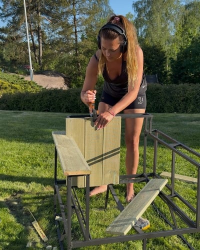 En kvinne som stifter fast kledning i tre til en stol. 
