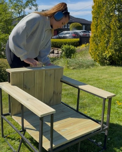 En kvinne som pusser over treverk på en stol ute i hagen.