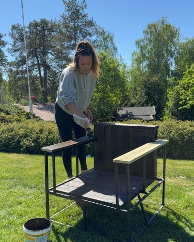 En kvinne som beiser en stol i en mørk beis ute i hagen.