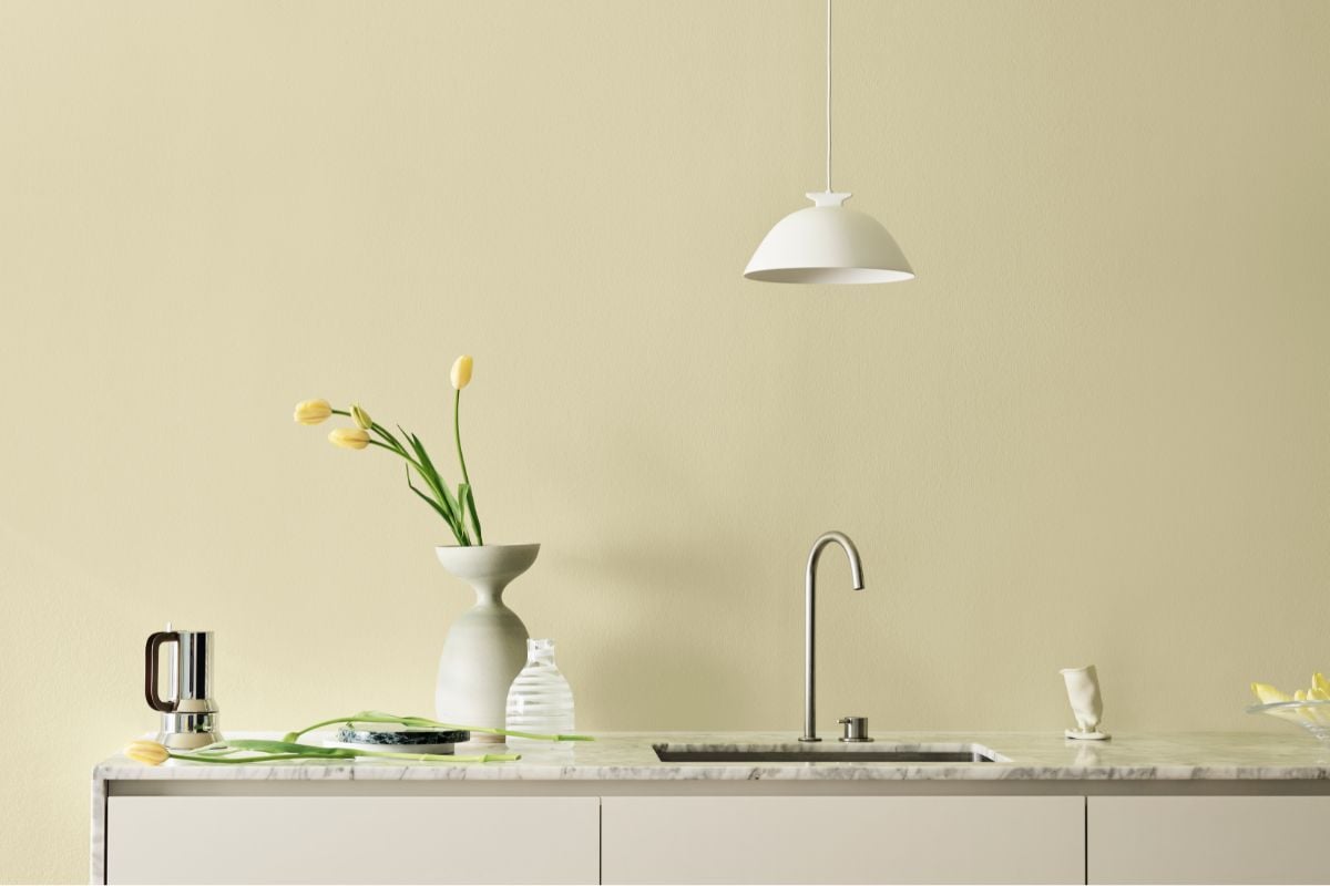 Kjøkken med beige-gul vegg, marmorbenk og minimalistisk dekor i Jotun-farge.