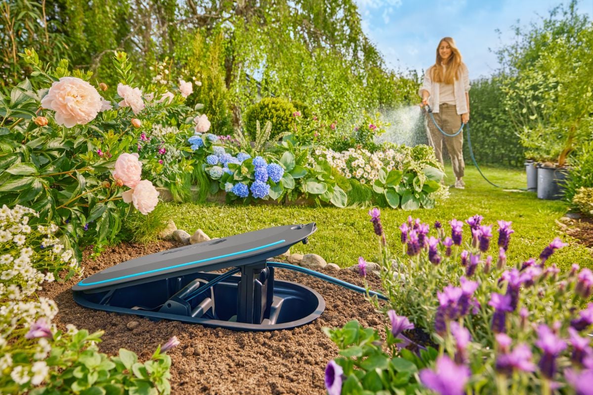 Kvinne vanner blomster med slange koblet til Gardena RollUp slangetrommel i hage