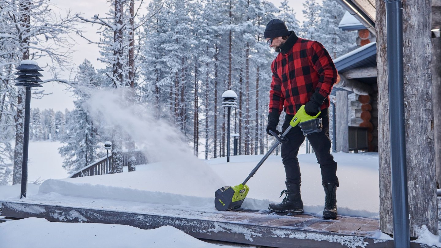 En person rydder snø fra en hytteveranda med en håndholdt snøslynge fra Ryobi.