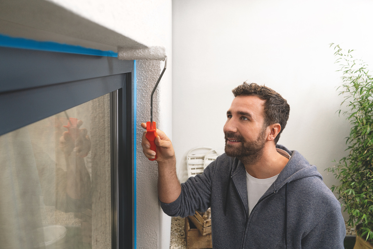 Mann som maler utenfor vindu ved siden av maskeringstape