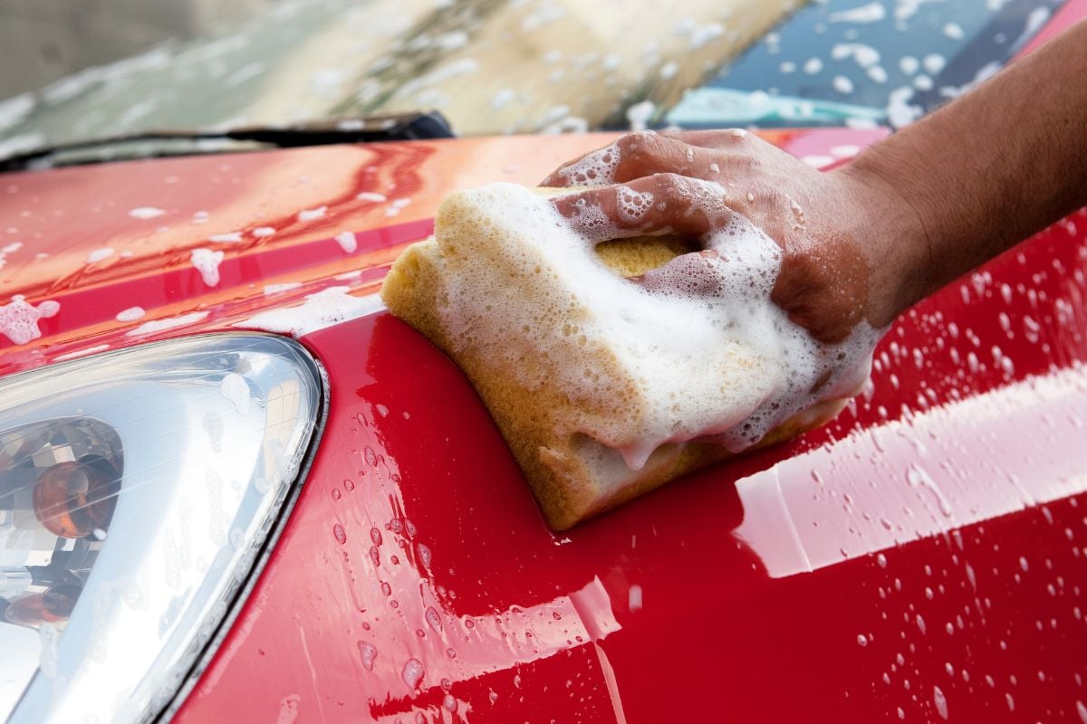 Nærbilde av at fronten på en rød bil vaskes med såpe og svamp