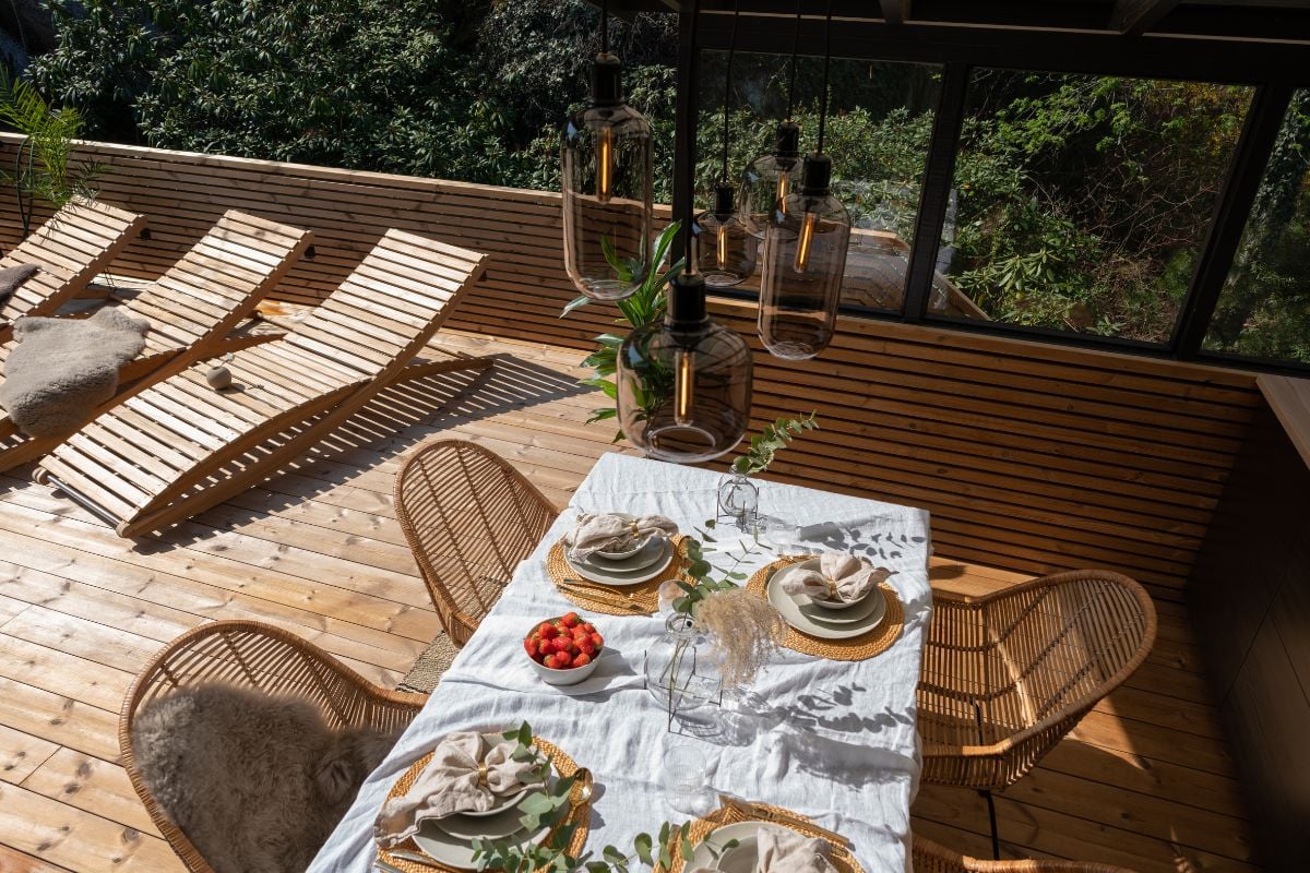 Solfylt terrasse med solsenger av tre, og dekket bord med hvit duk