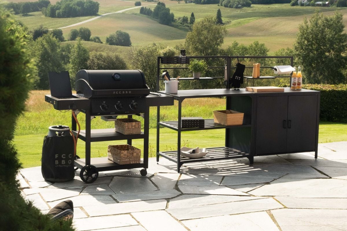 Stor grill og utekjøkken med utsikt til åker og skog, plassert på flislagt terrasse.