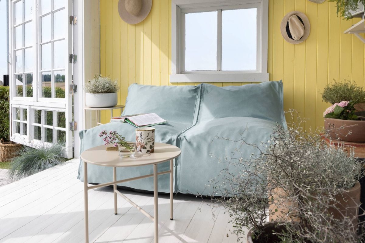 Blå utesofa foran solgul vegg med lite bord foran