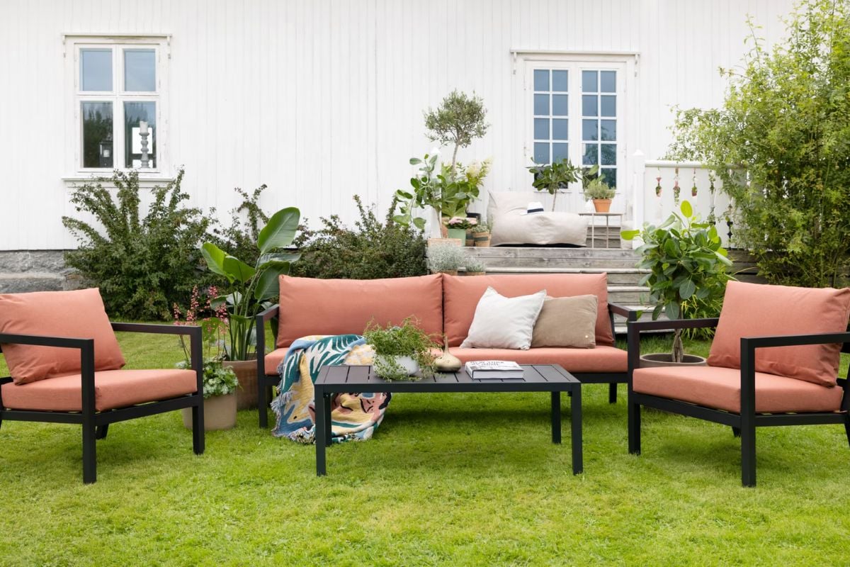 Sofagruppe med rustfargede puter foran hvitt hus