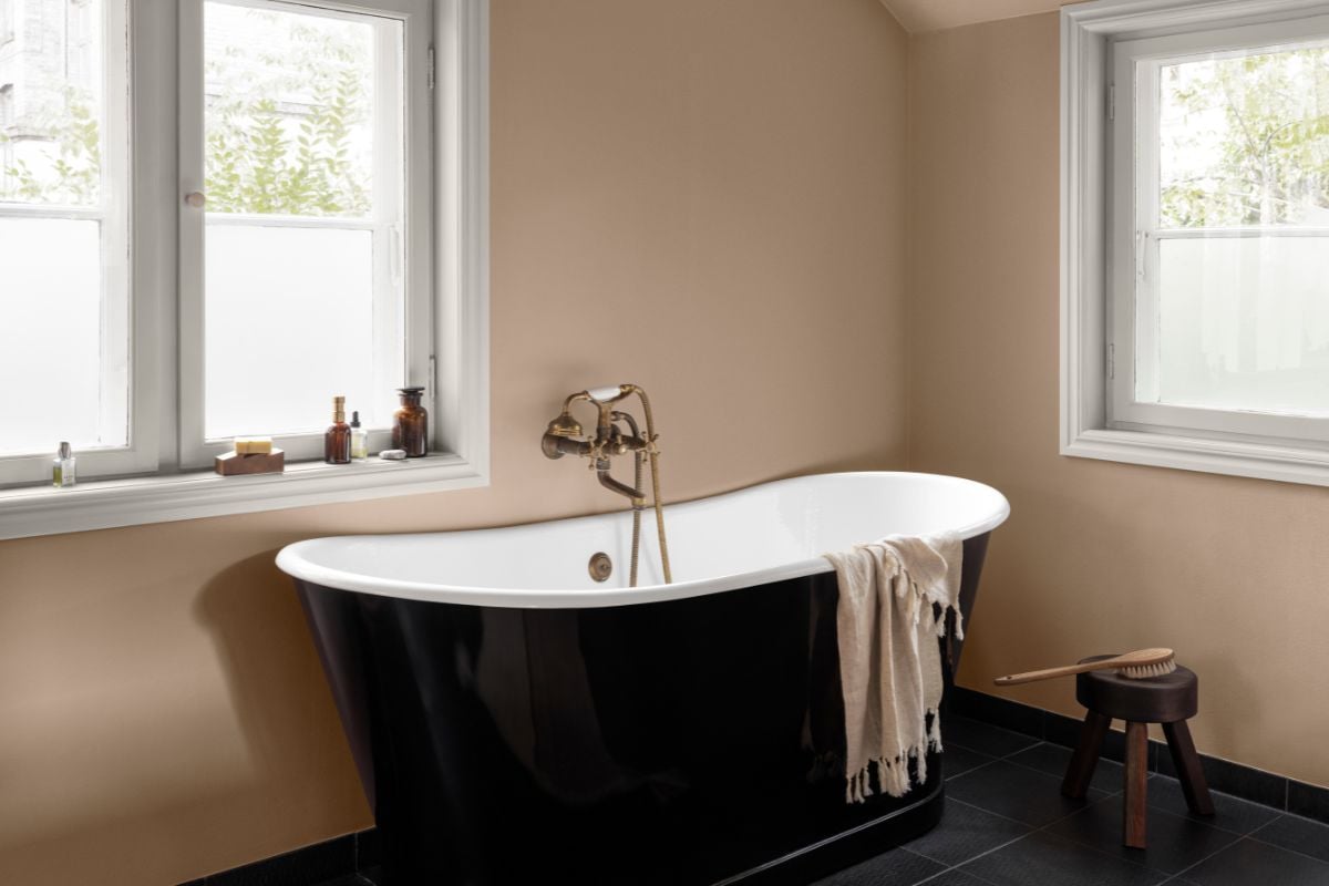 Frittstående sort badekar i rom med store vinduer og lyse matte vegger.
