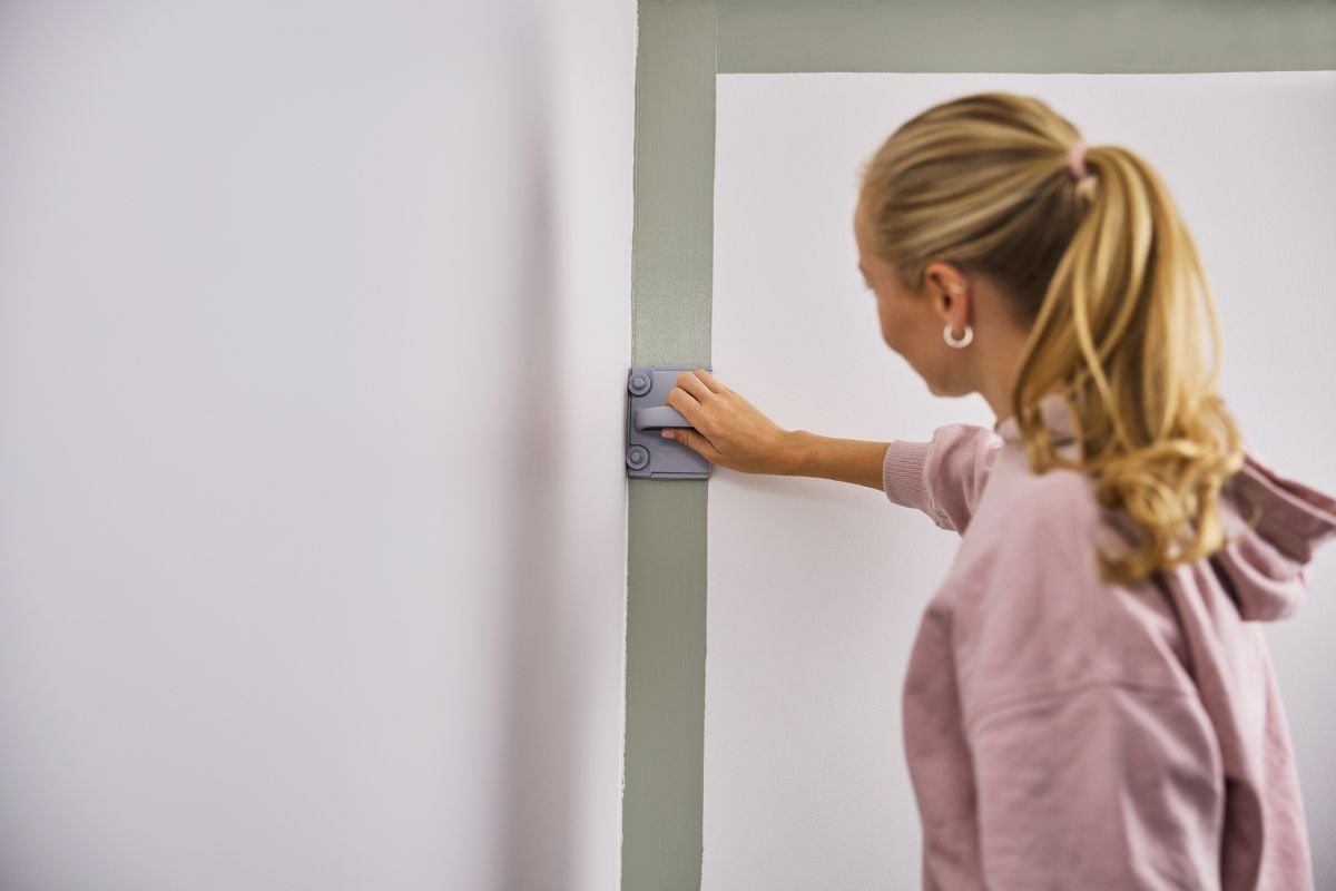 Kvinne maler rette linjer langs veggen med malepute.