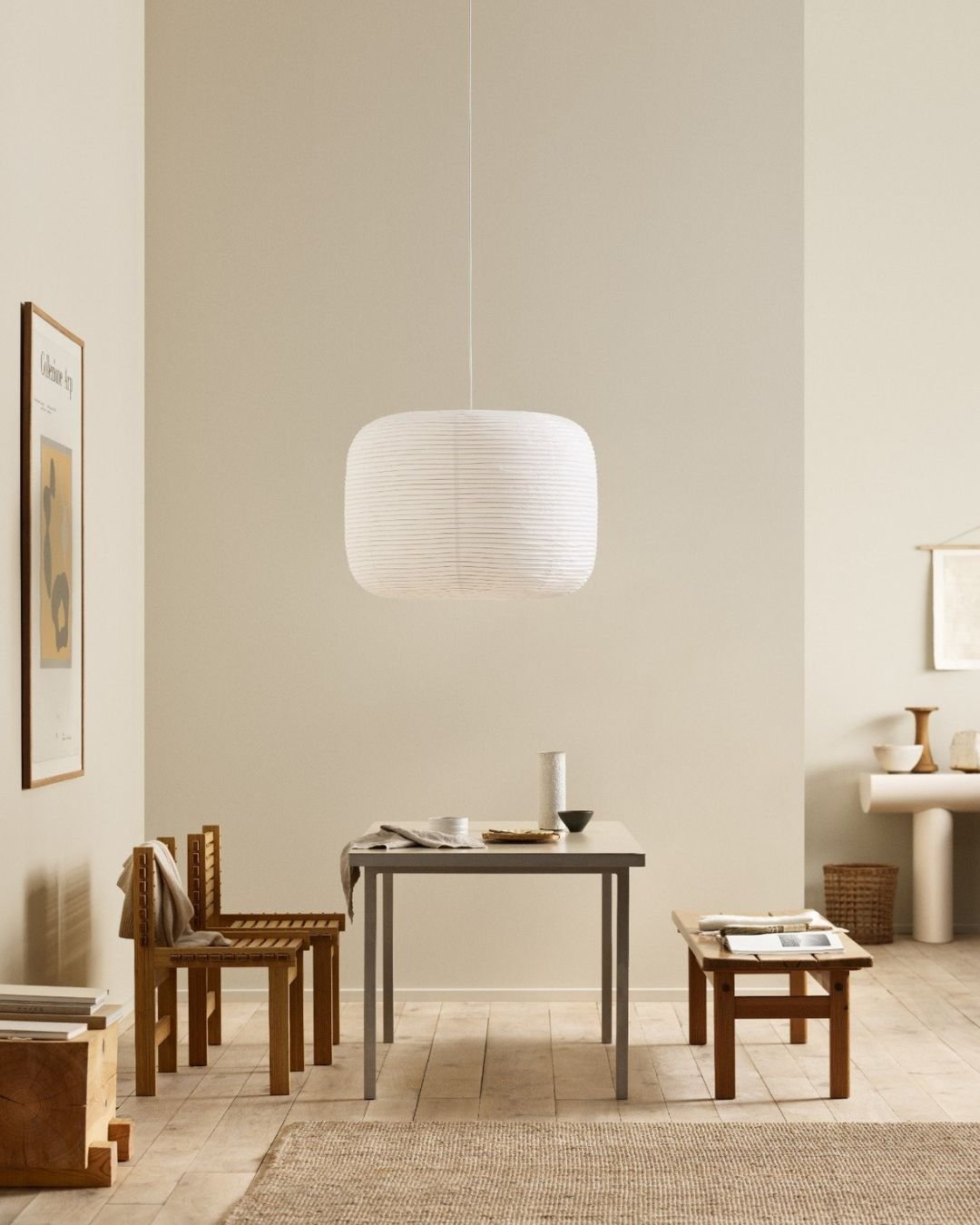 Lyst rom med grått bord, trestoler og benk, nøytrale vegger og en stor hvit taklampe som henger midt i rommet.