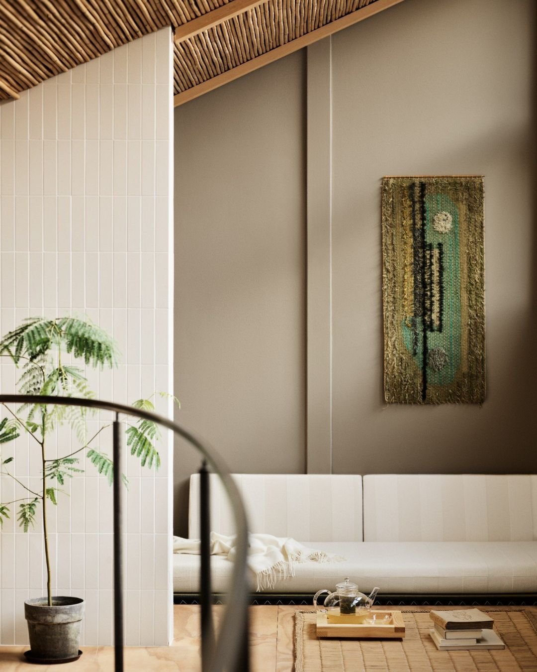 Stue med grå og hvite vegger, hvit sofa, grønn plante i potte og veggteppe i grønne nyanser.
