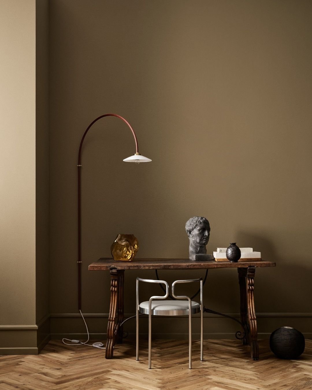 Rom med olivengrønne vegger, mørkt trebord, metallstol og dekor som skulptur, vase og lampe.