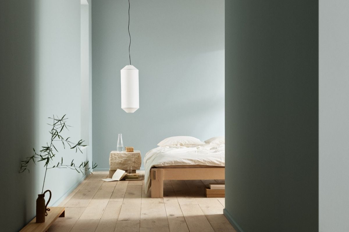 Soverom med lyseblå vegger, enkel tre­seng med hvitt sengetøy, stein nattbord og hengende hvit lampe.