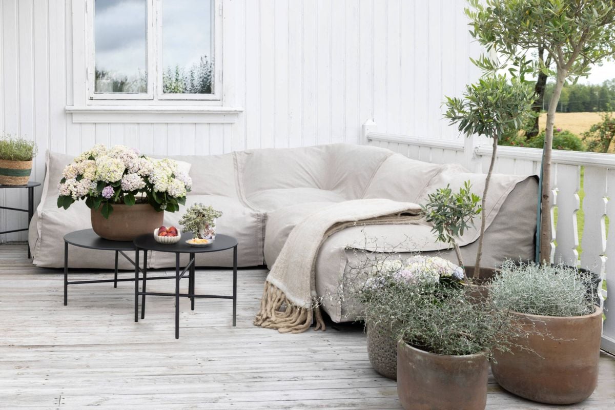 Utesofa og kaffebord med puter og potteplanter på terrasse mot hvit vegg.