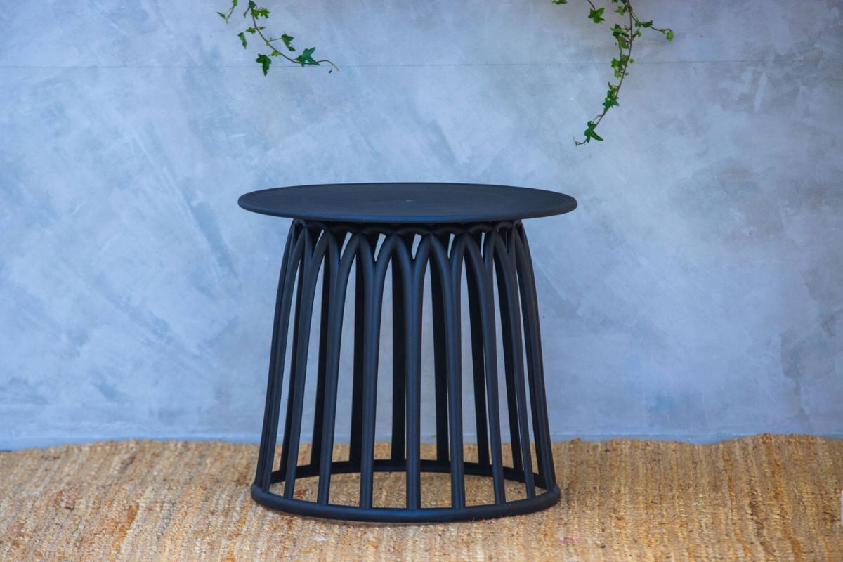 Rundt sort sidebord i plast på liten uteplass med blå vegg og naturlig teppe