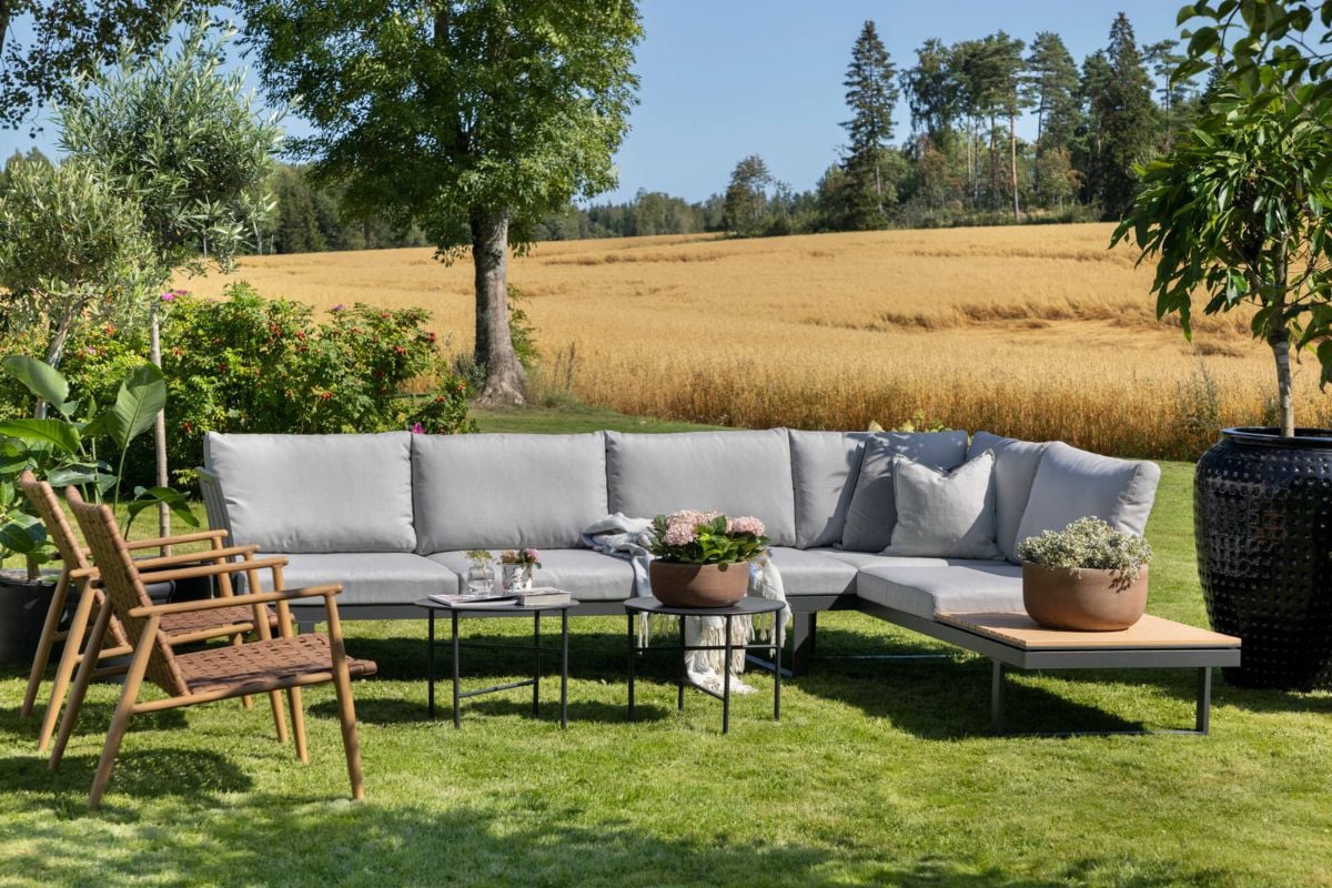 Grå loungegruppe og to små bord på en større uteplass med utsikt over eng