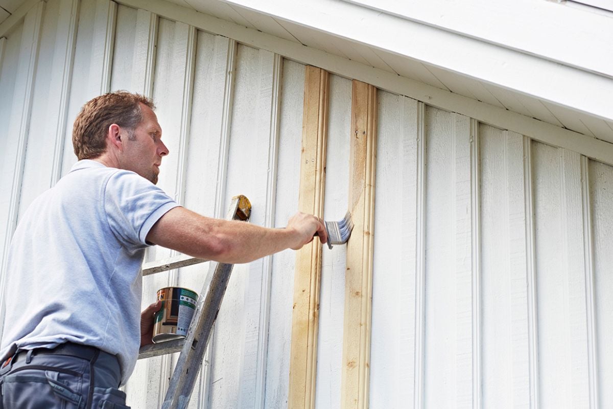 Mann står på stige og maler husvegg hvit
