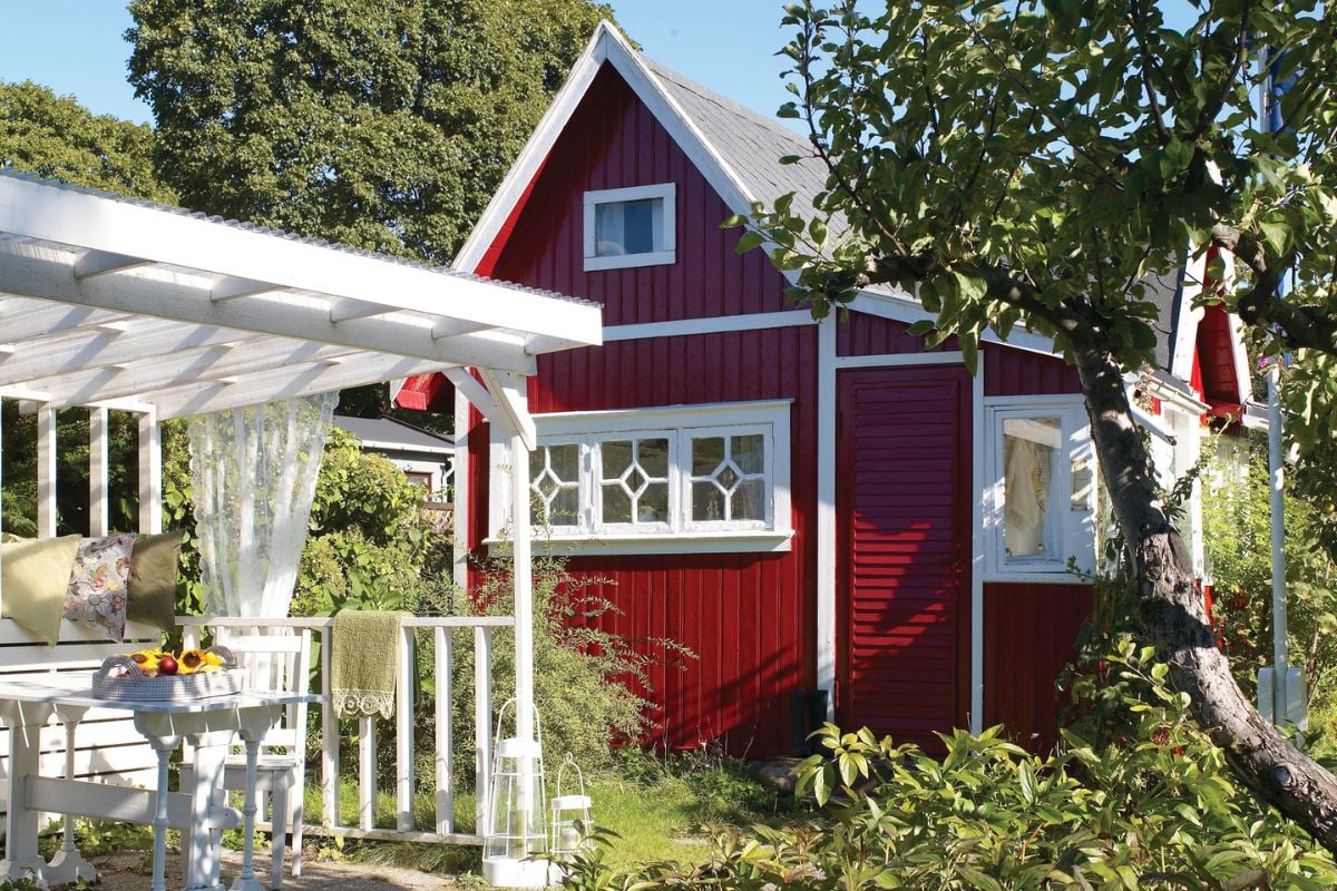 Et rødt hus med hvite rammer i grønne omgivelser