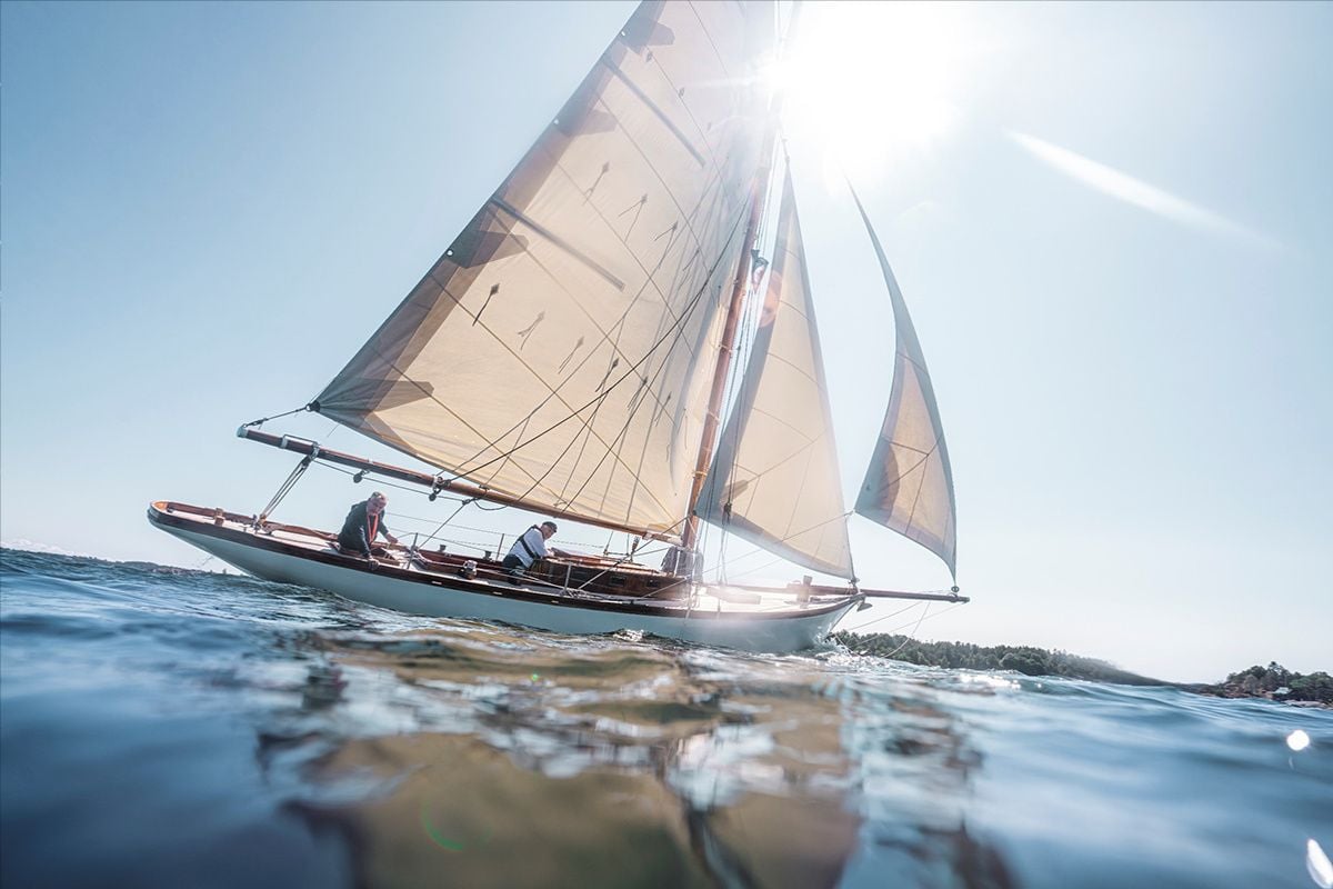 Seilbåt i medvind på havet med lav sol og speiling i vannet.