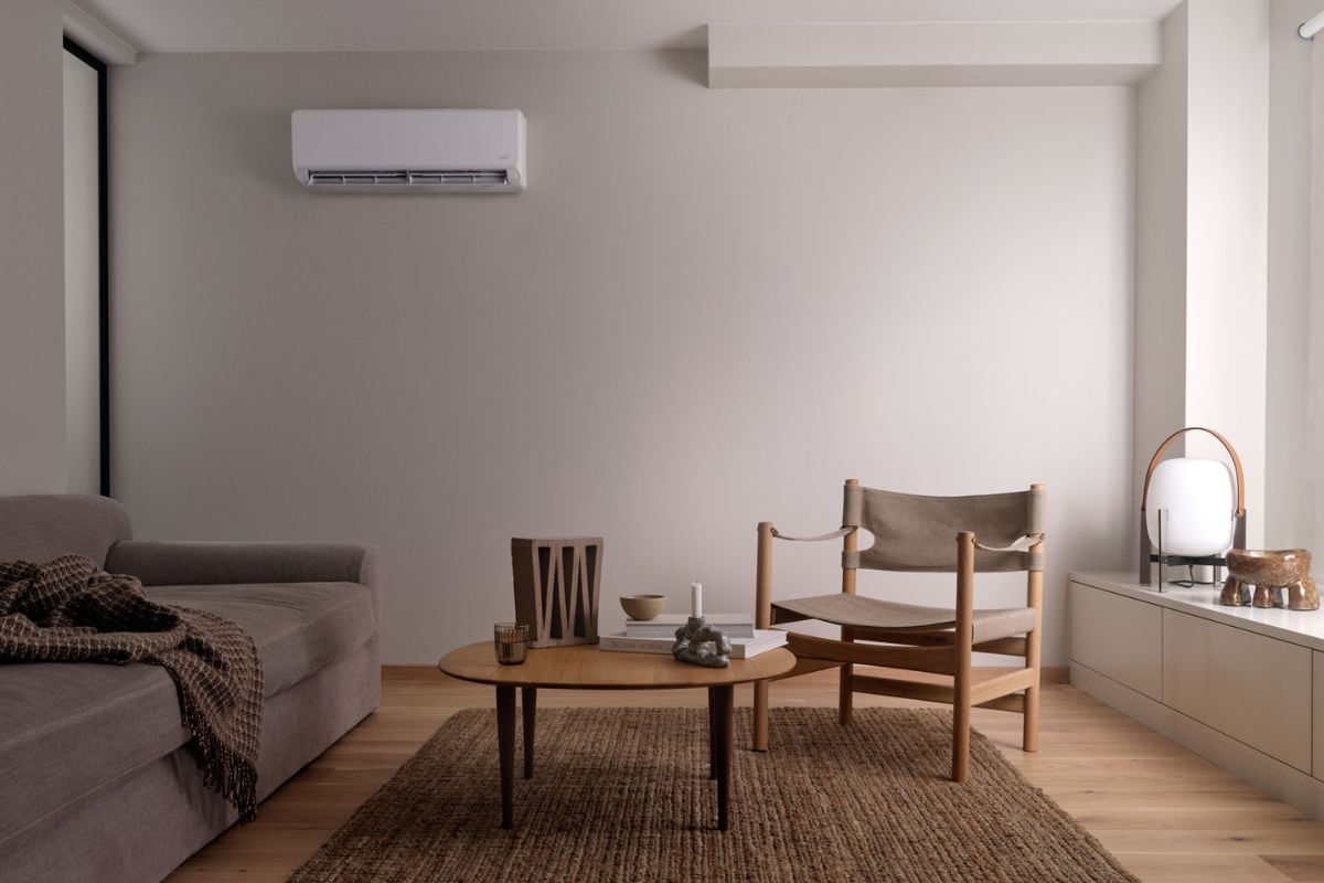 Hvit varmepumpe hengende på veggen, i en stue innredet med møbler og detaljer i jord-toner.