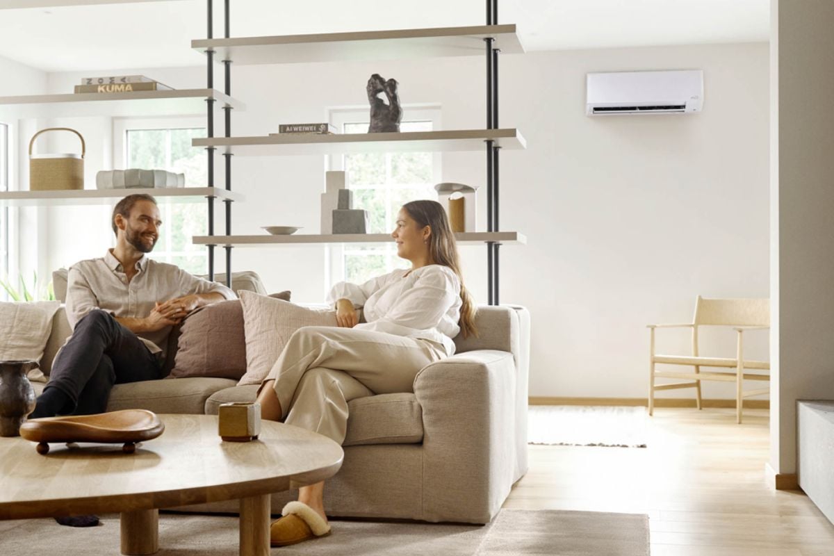 Stuerom med et par I sofaen, og en hvit varmepumpe på veggen bak