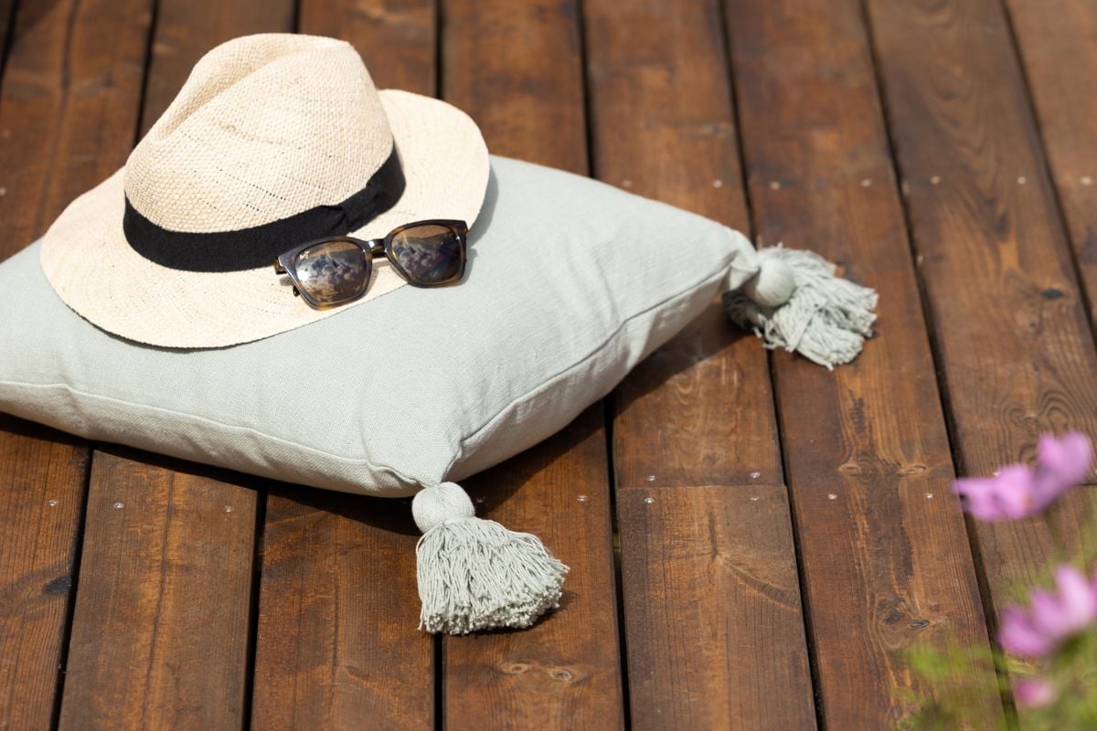 Hatt og solbriller på en pute med dusker, liggende på en terrasse i tre.