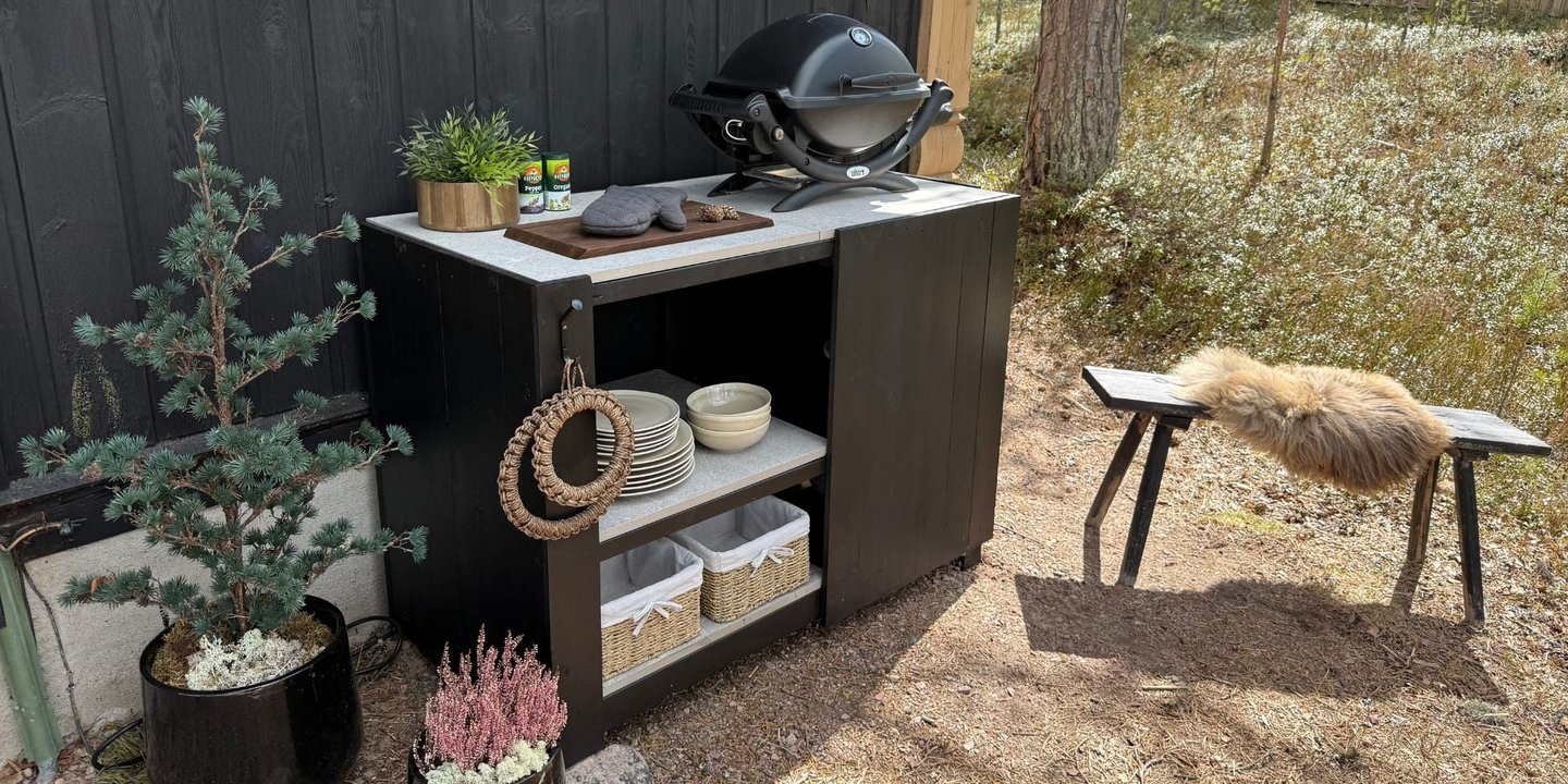 Ferdig stylet utekjøkken med grill og servise på innsiden. En plante på venstre side.