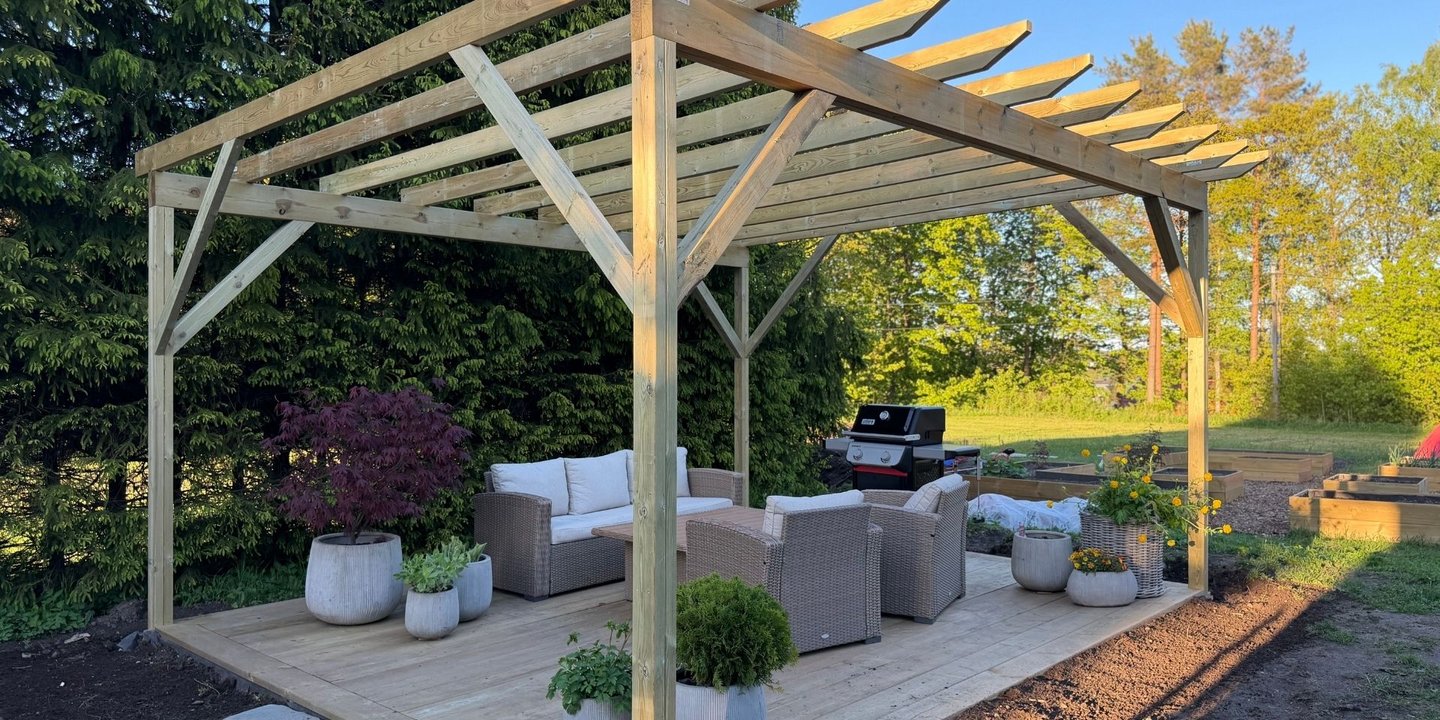 Resultat av ferdig pergola over platting med møblement og planter.