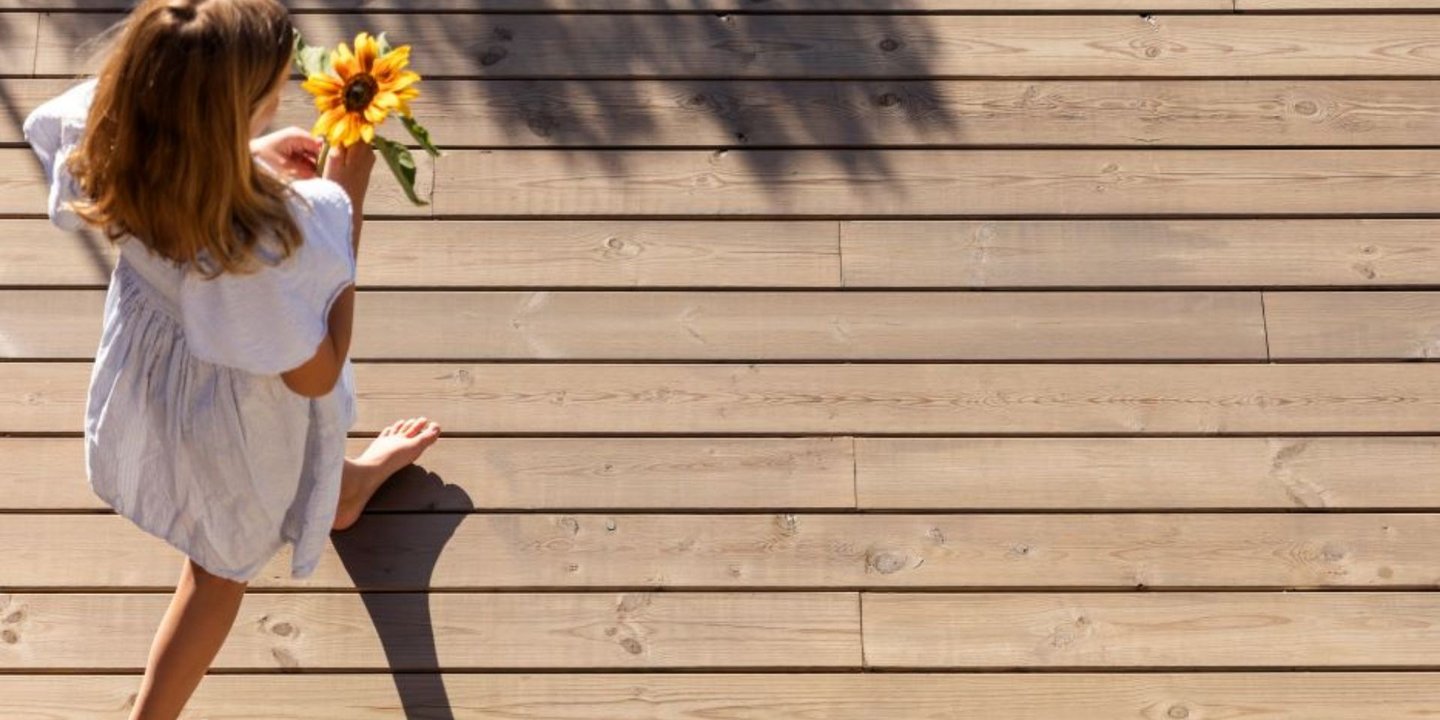 Jente i hvit kjole en solfylt dag, med solsikkeblomster i hånda går over terrassen.