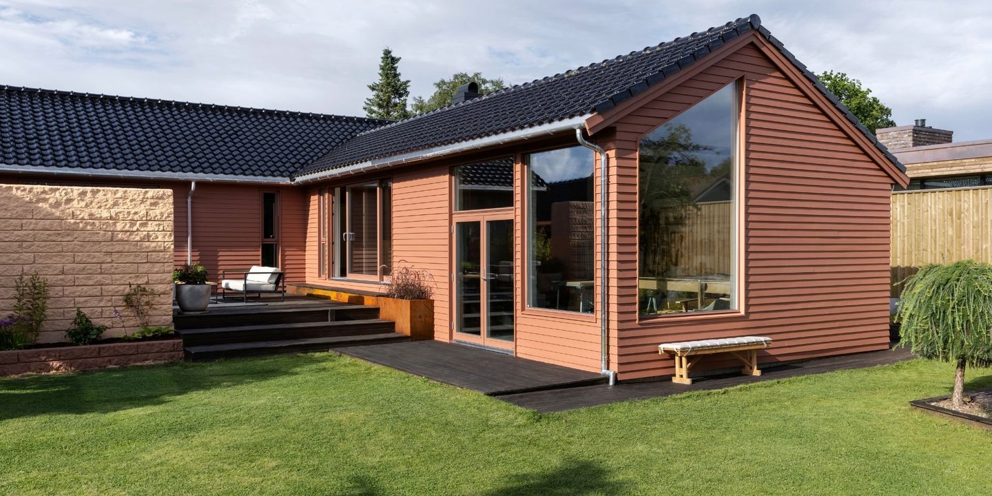 Hus malt i dus rødfarge, med grønn gressplen foran på en overskyet dag.