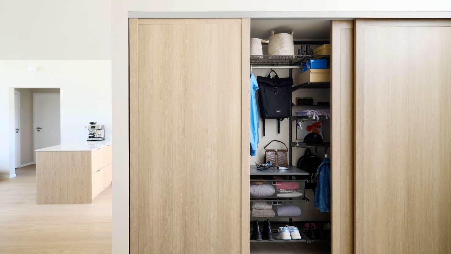 Skyvedørsgarderobe i lyst treverk og organisert innhold.