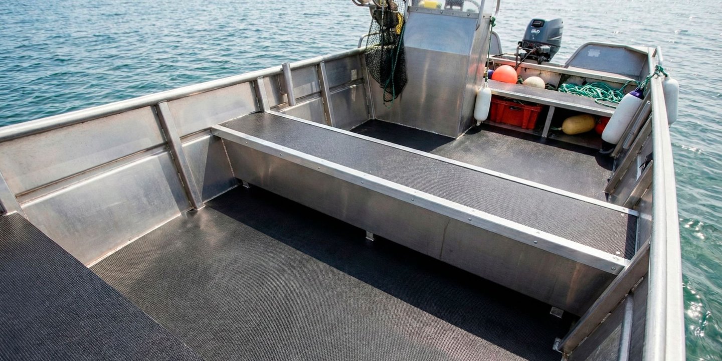 Båt på vannet med fokus på gulvet i båten, som er en svart, slitesterkplate fra gop