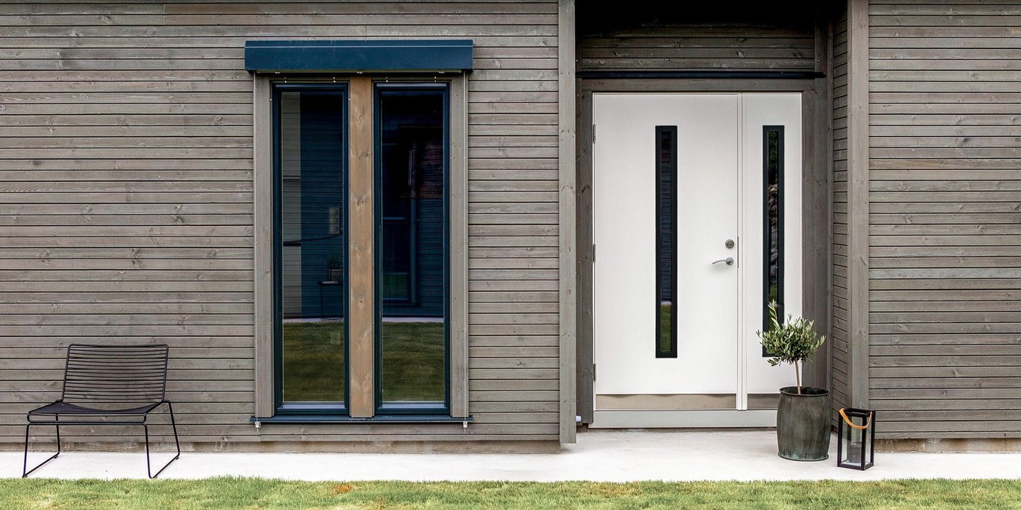 Hvit ytterdør, bilde tatt utendørs. Det er en gressplen og fliser lagt foran inngangspartiet.