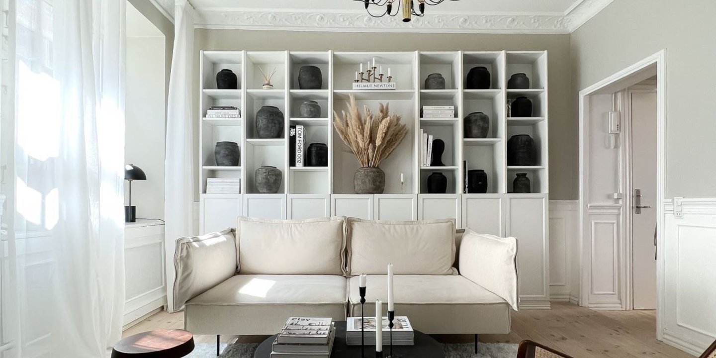 En klassisk stue med stukkatur og beige vegger. En sofa er plassert midt i rommet og en bokhylle er plassert bak.
