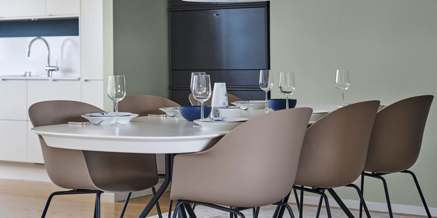 En spisestue med seks stoler, plassert på et grått gulvteppe. Veggene er malt grønne. 