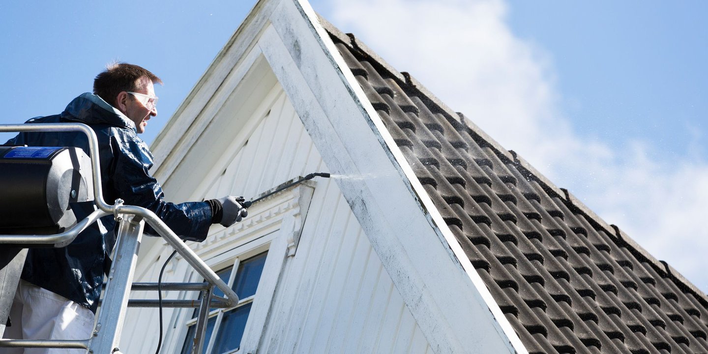 Mann står på stige og bruker produkter fra Jotun til å vaske et hvit hus