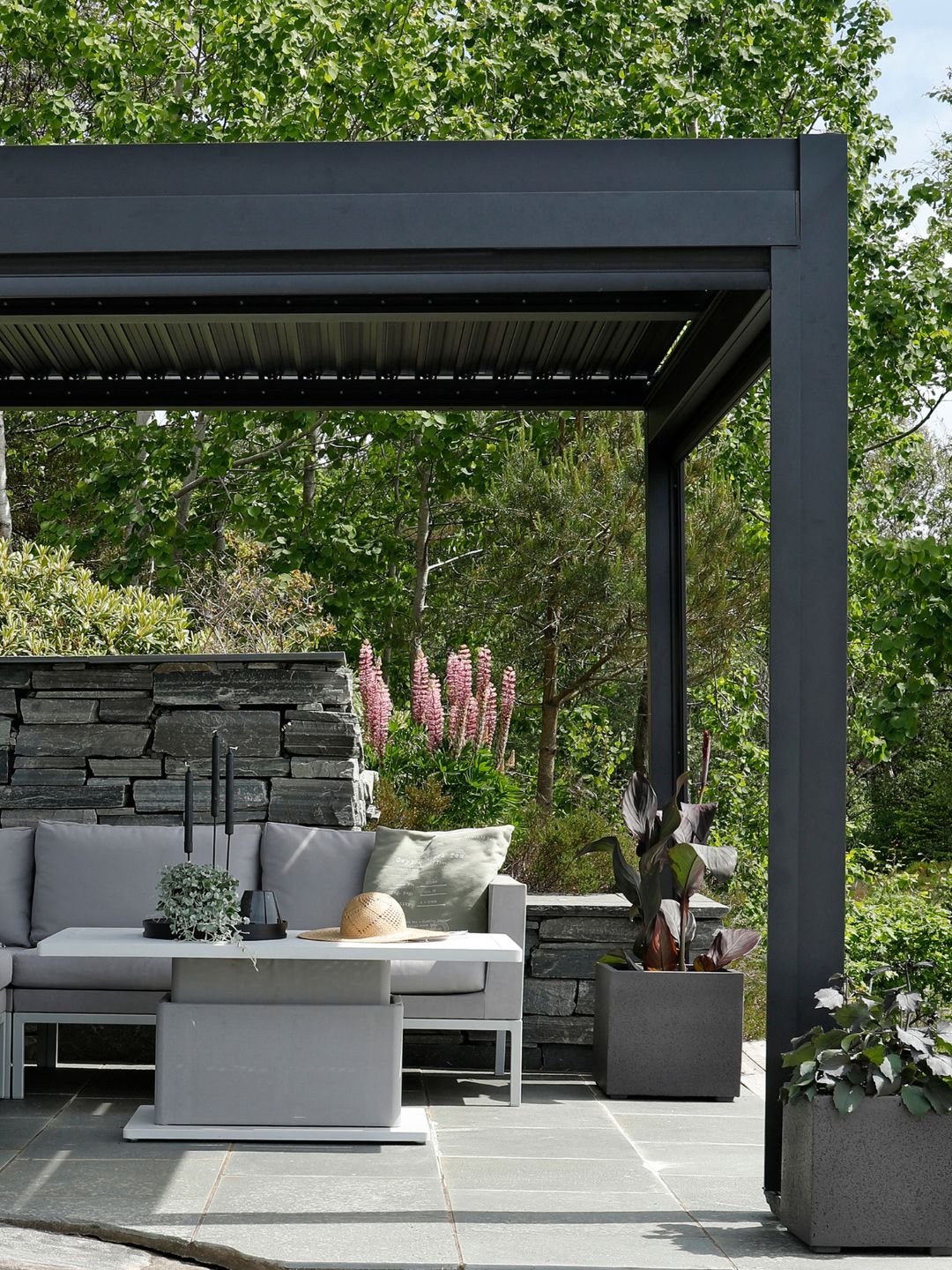En svart pergola med en grå sofagruppe under.