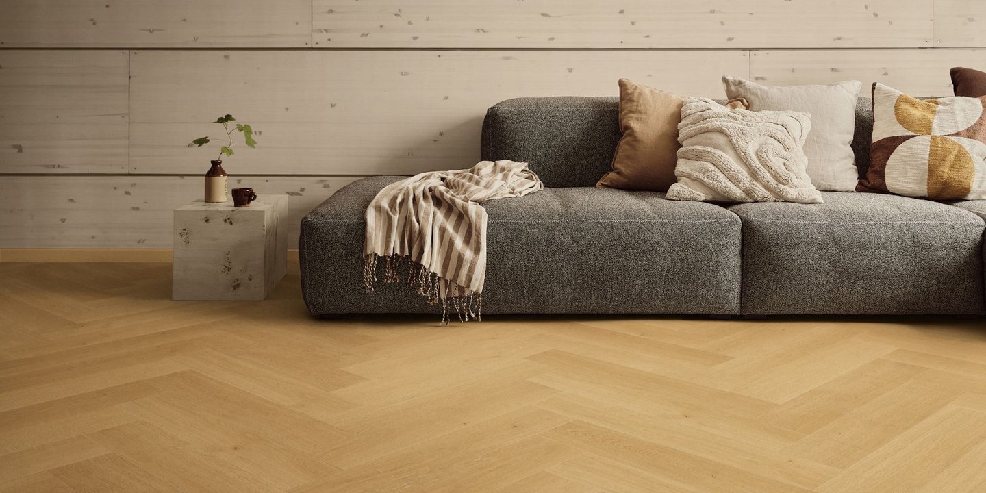 Stue med sofa og et sidebord på et lysebrunt fiskebensgulv.