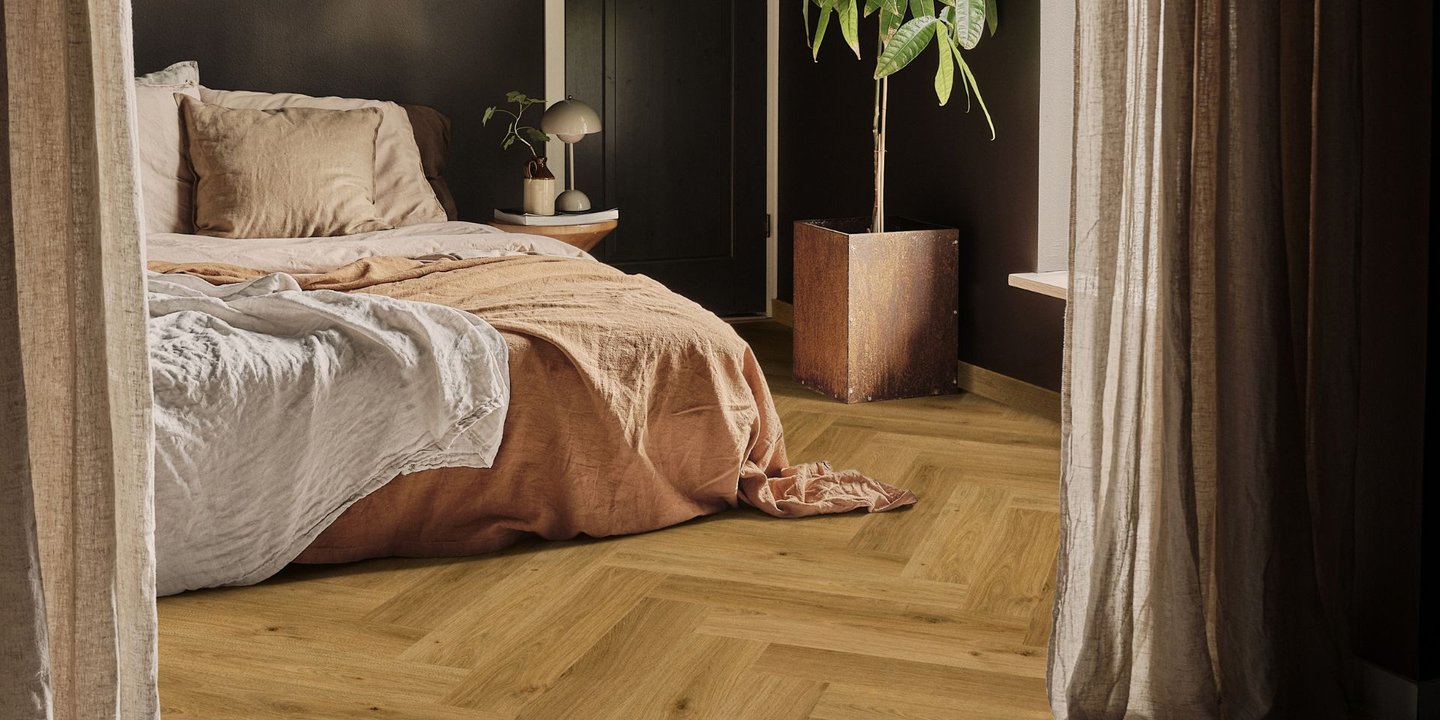 Et soverom med en seng og en plante. Veggene er svarte og fiskebensgulvet er mellomlyst brunt.