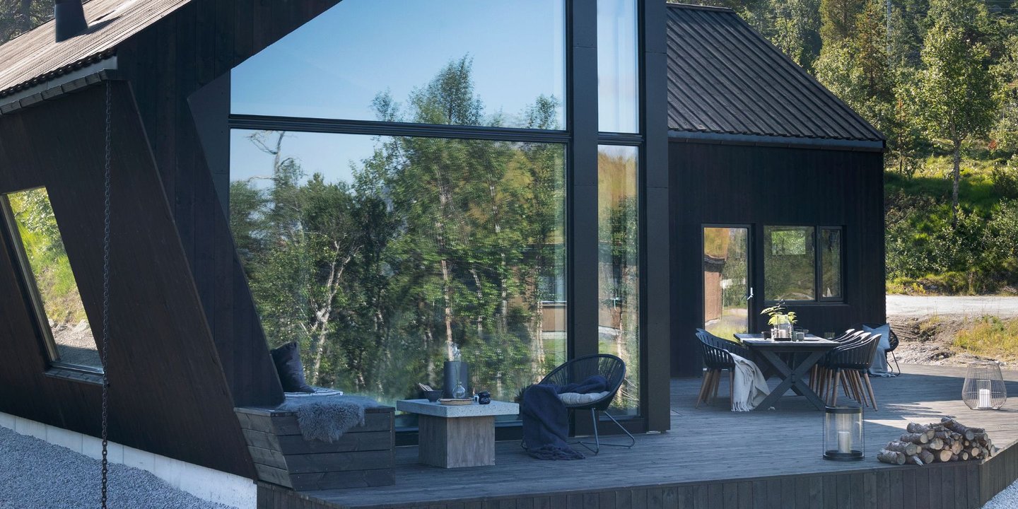Matt beis gir et rolig og eksklusivt uttrykk. Her er den moderne hytta beiset i en mørkbrun farge. Veggene har store vinduer med en uteplass foran seg.